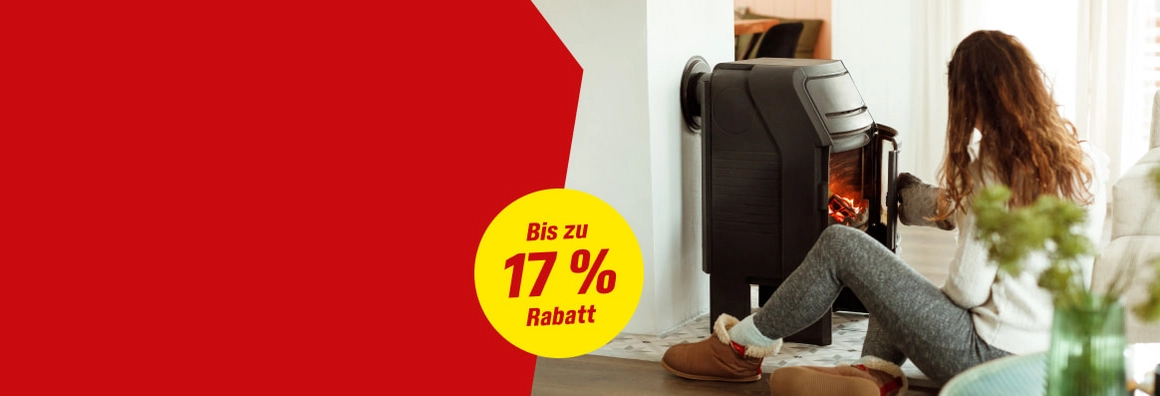 Person sitzt vor einem brennenden Kaminofen und öffnet dessen Tür.